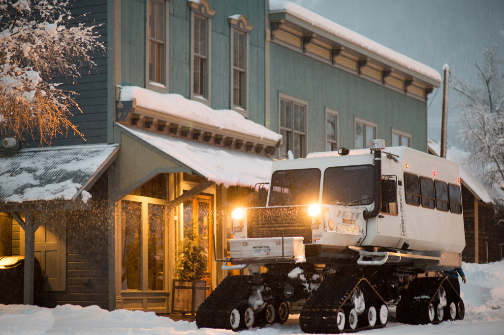 A snowcat with it's light on sits outside of the historical Eleven Scarp Ridge Lodge.